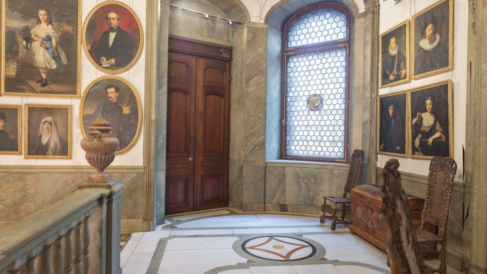 The Upper Vestibule: marble floor with inlaid medallions, a carved double door and walls of ancestral portraits