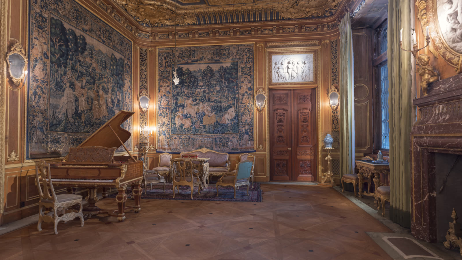 The Great Drawing Room: tapestries, gilt panelling, a grand piano and a carved double door under a stucco relief